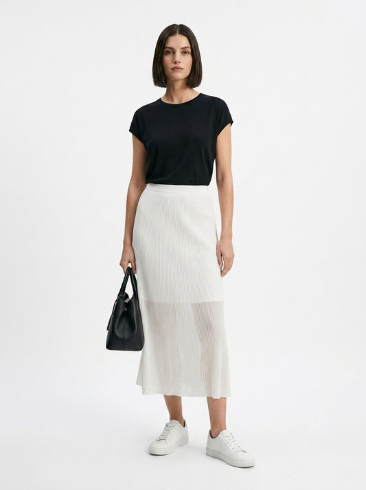Woman wearing a black top and white skirt holding a black handbag on a white background
