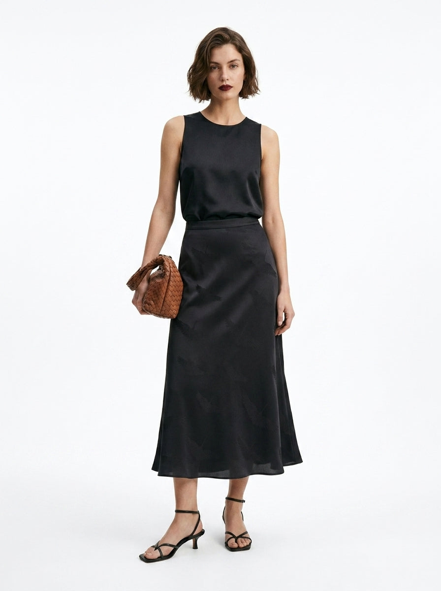 Woman wearing a black sleeveless top and skirt with a brown handbag on a white background