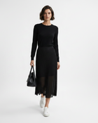 Woman wearing a black outfit with a sheer skirt holding a black handbag on a white background