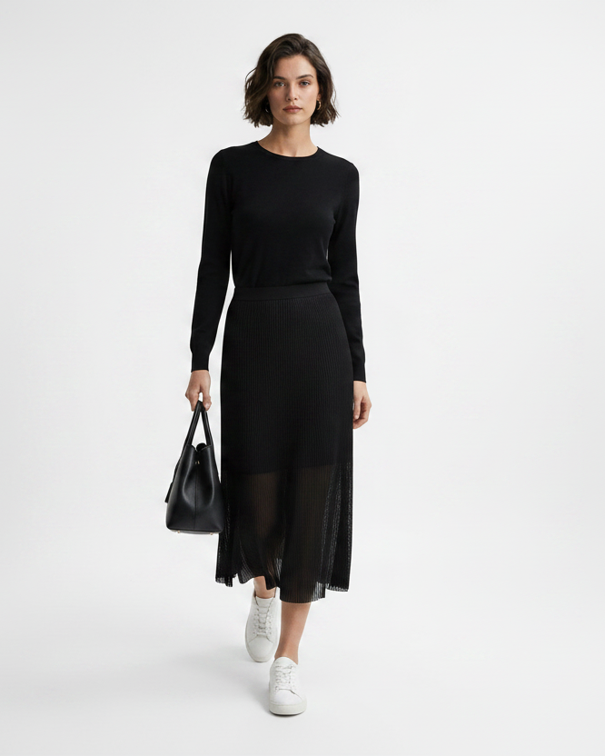 Woman wearing a black outfit with a sheer skirt holding a black handbag on a white background