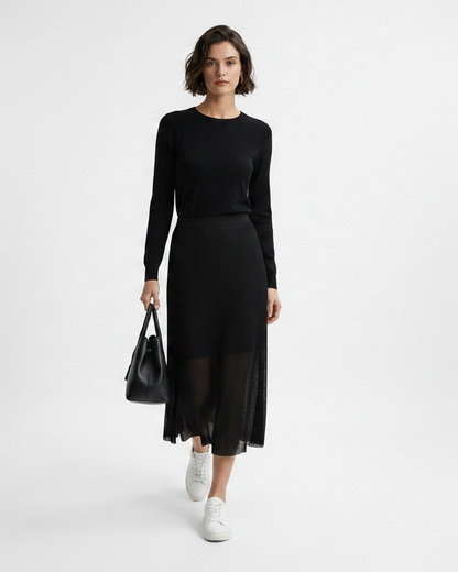 Woman wearing a black outfit with a sheer skirt holding a black handbag on a white background