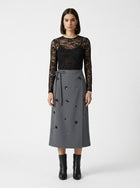 Woman wearing a black lace top and gray skirt with black buttons on a white background
