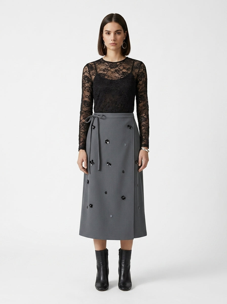 Woman wearing a black lace top and gray skirt with black buttons on a white background