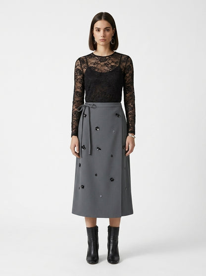 Woman wearing a black lace top and gray skirt with black buttons on a white background