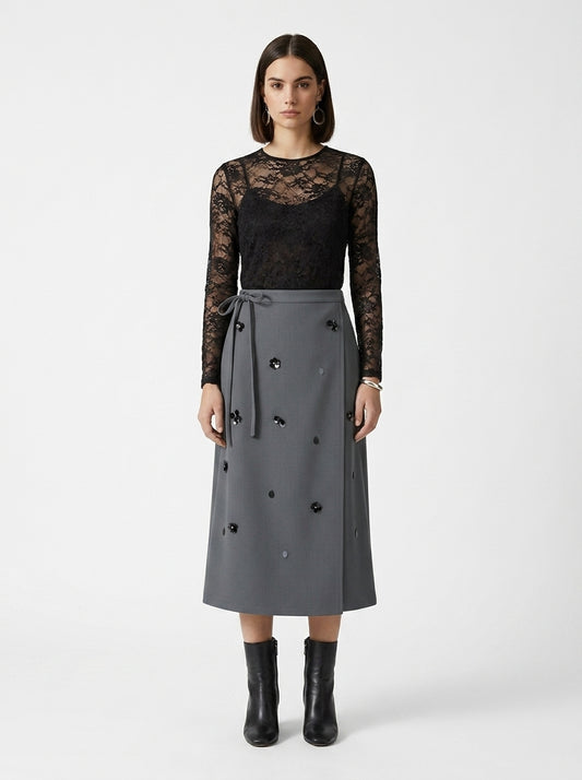 Woman wearing a black lace top and gray skirt with black buttons on a white background