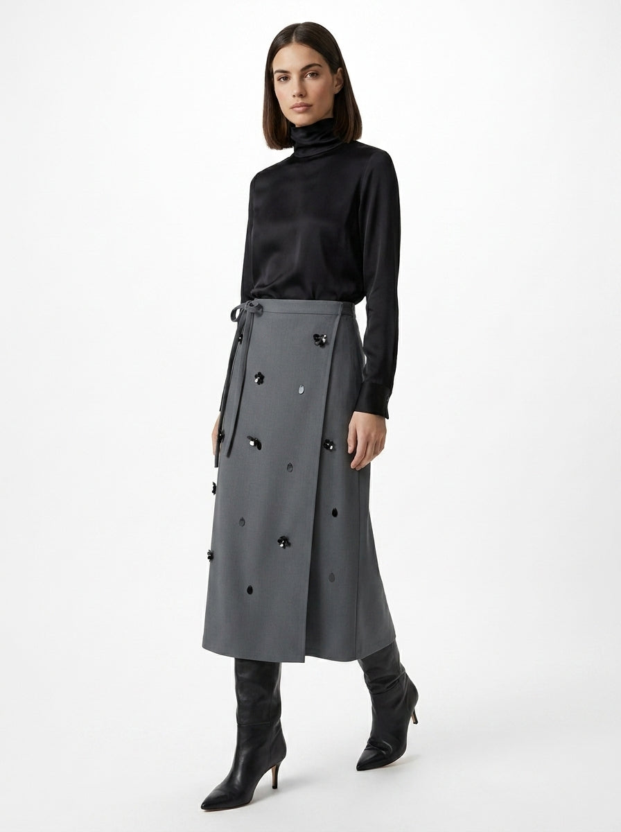 Woman wearing a black turtleneck and gray skirt with black buttons on a white background