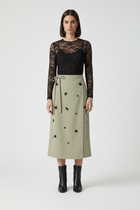 Woman wearing a black lace top and beige skirt with black embellishments on a white background