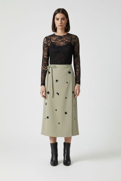 Woman wearing a black lace top and beige skirt with black embellishments on a white background