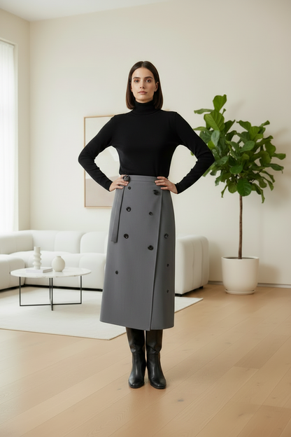 Woman in a black turtleneck and gray skirt standing in a modern living room.