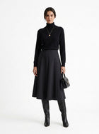 Woman wearing a black turtleneck, black skirt, and black boots on a white background