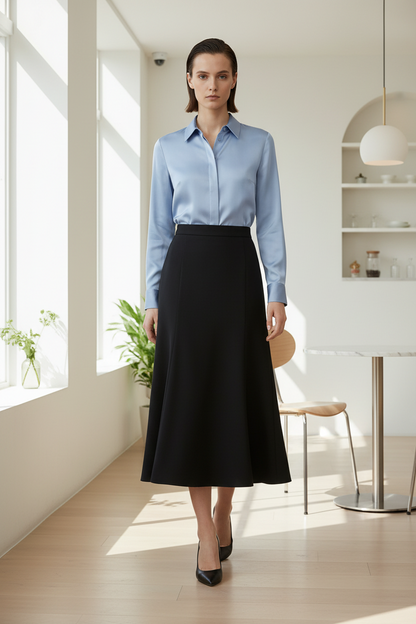 Woman wearing a light blue shirt and black skirt in a bright room with large windows.