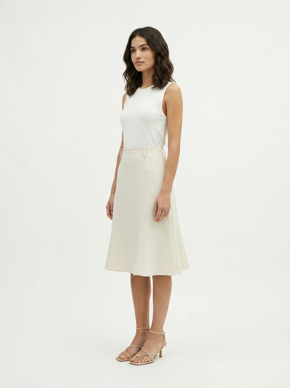 Woman wearing a white sleeveless top and cream skirt on a plain background
