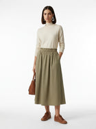Woman wearing a beige turtleneck and green skirt with brown shoes on a white background