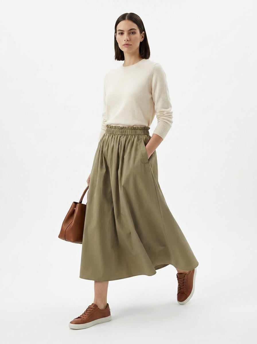 Woman wearing a white sweater and green skirt with brown shoes and bag on a white background
