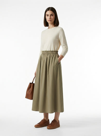 Woman wearing a beige sweater and green skirt with brown shoes and bag on a white background